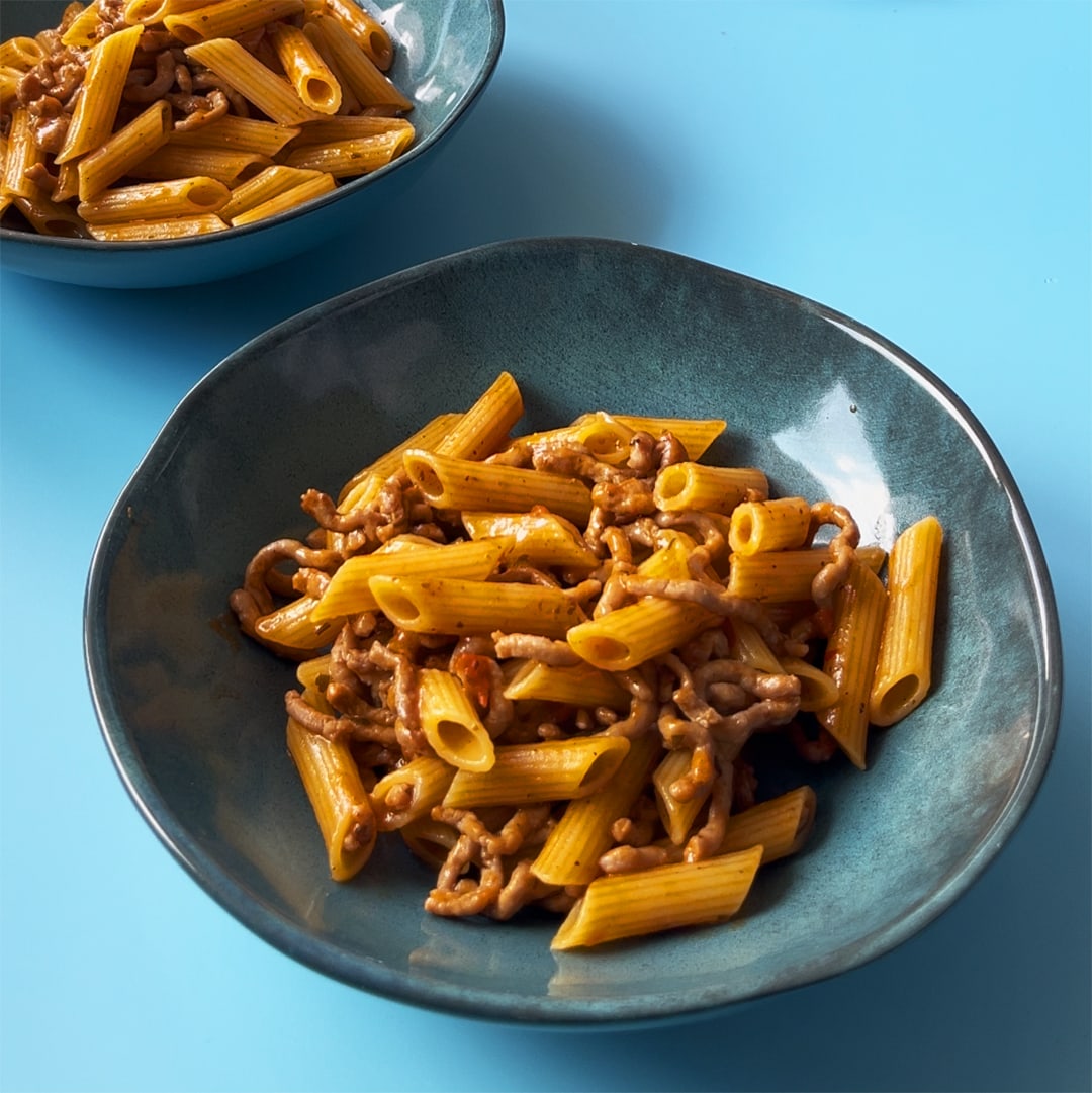 A plate of penne puttanesca with beef on a blue background
