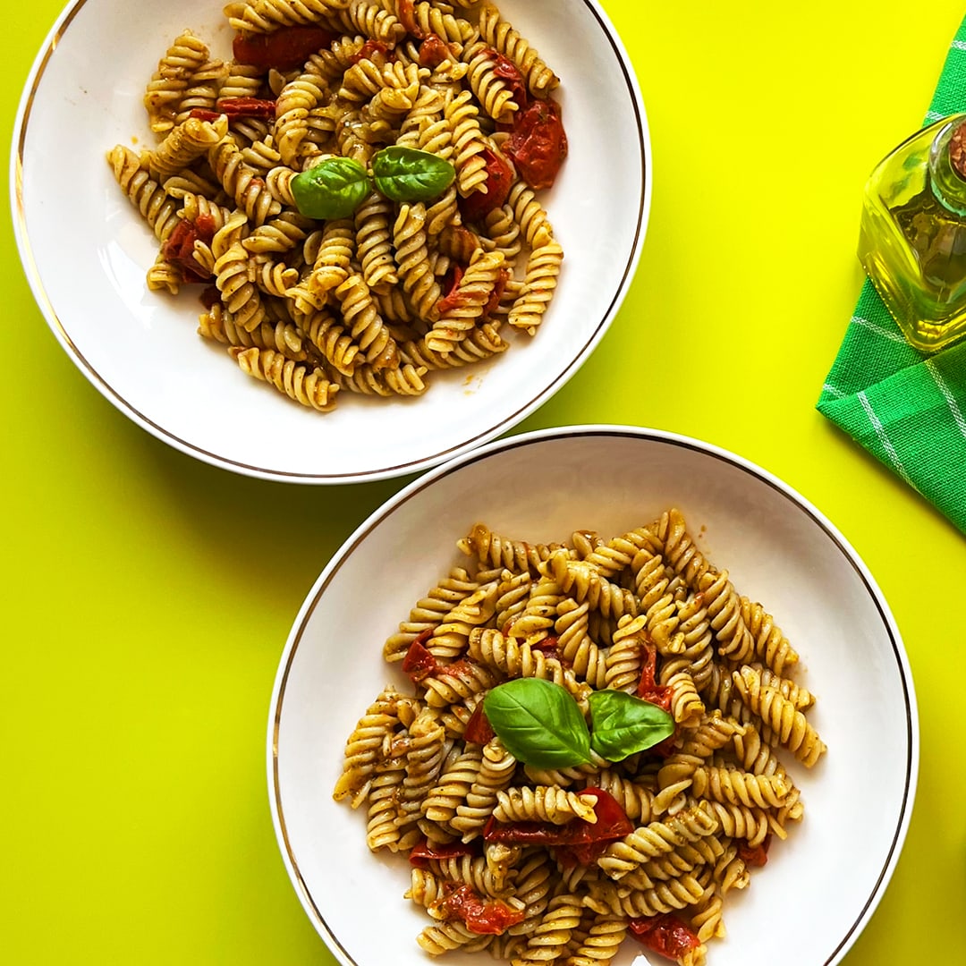 Two dishes of Pesto Tomato Pasta with Cherry Tomatoes on green background