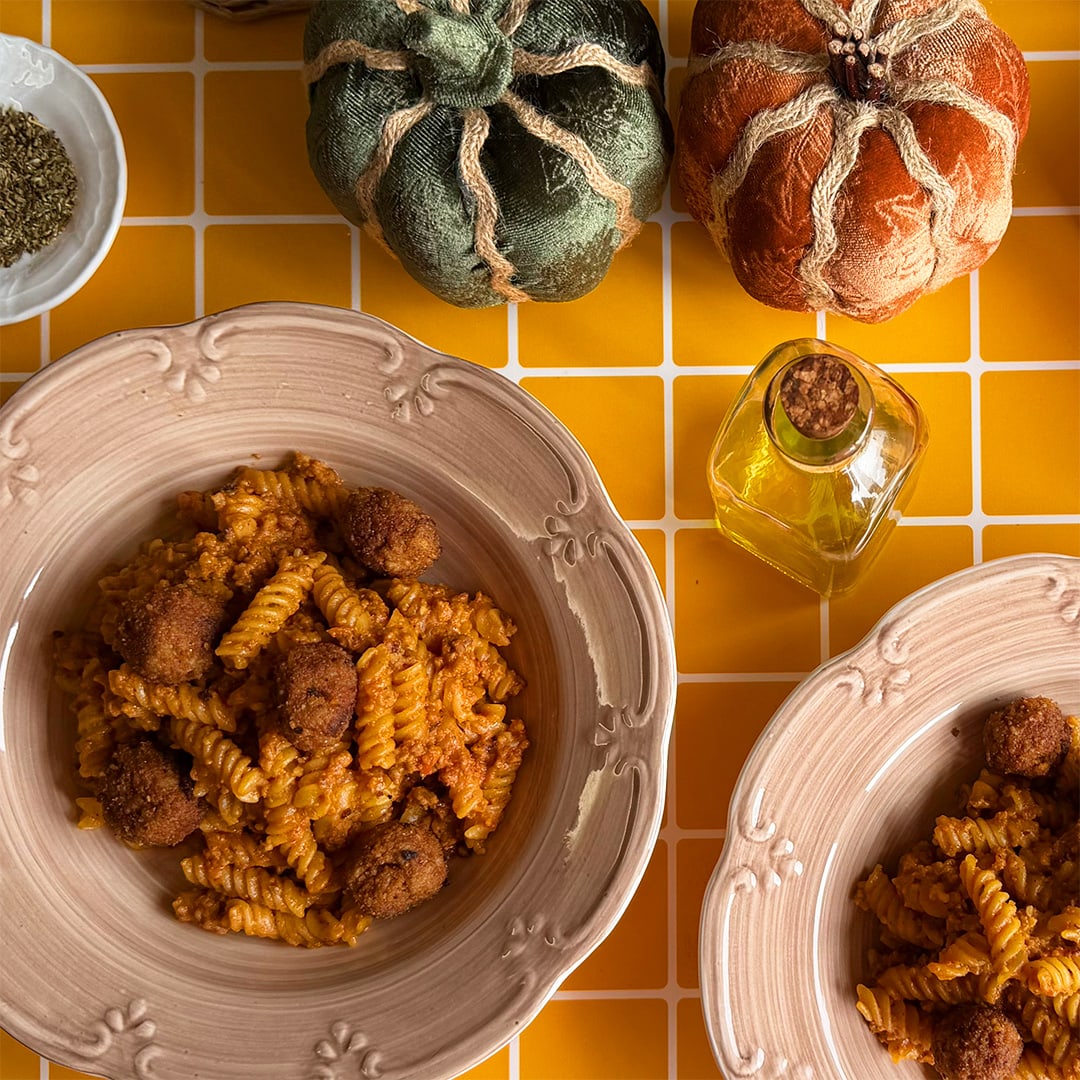 Two plates of pasta with meatballs and tomato sauce against an orange background, decorated with fall motifs. 