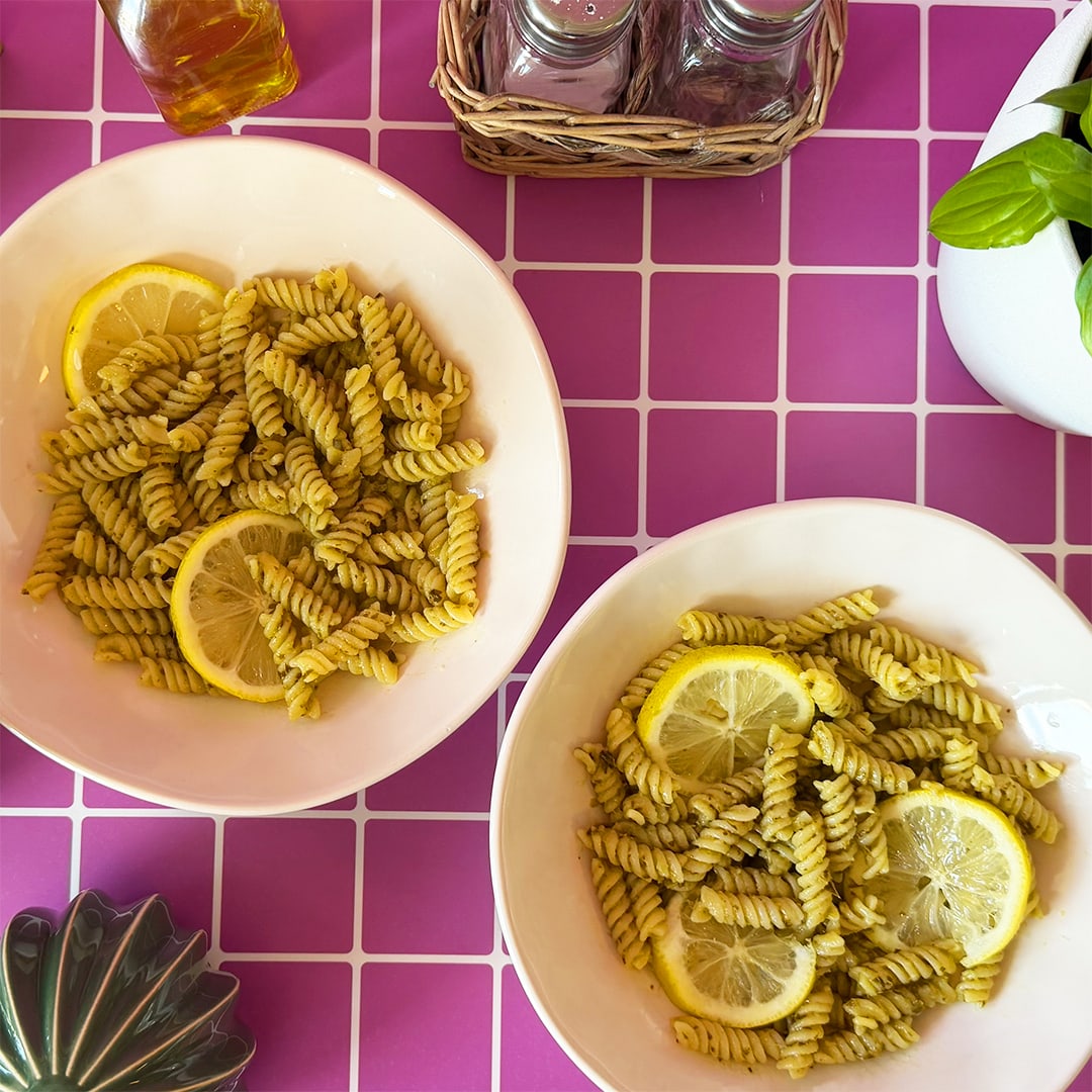 Two plates of lemon pesto pasta on a lilac background