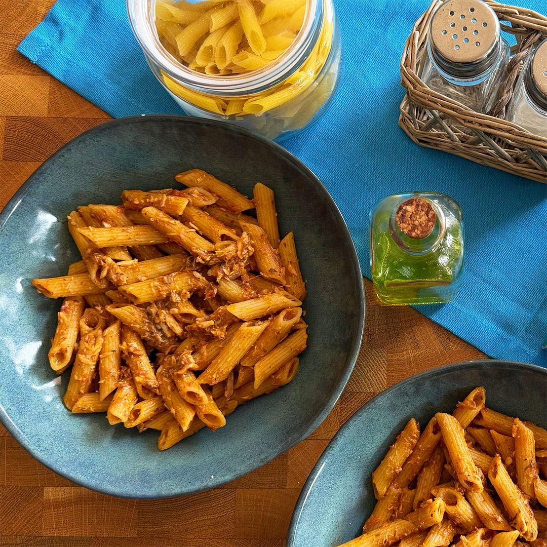 Two plates of anchovy pasta and puttanesca sauce on a set table